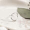 Single open circle sterling silver ring on white marbled dish with green leaf.

